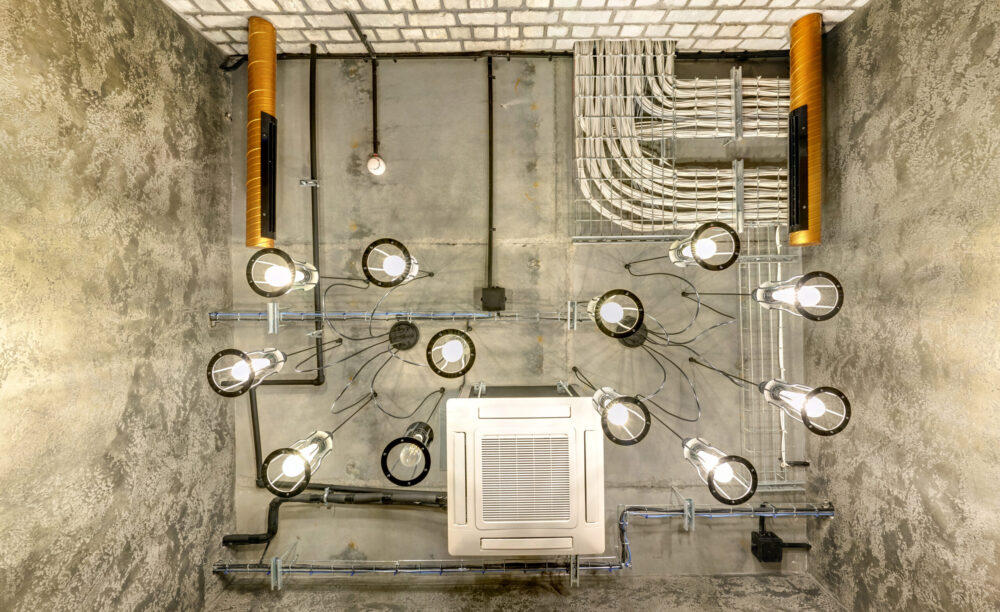 looking up on gray concrete ceiling with halogen spots and edison lamps in loft office room with air conditioning and orange ventilation pipe