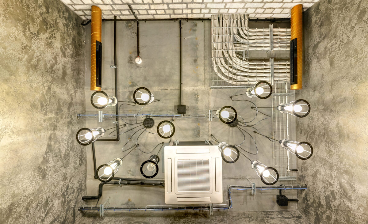 looking up on gray concrete ceiling with halogen spots and edison lamps in loft office room with air conditioning and orange ventilation pipe